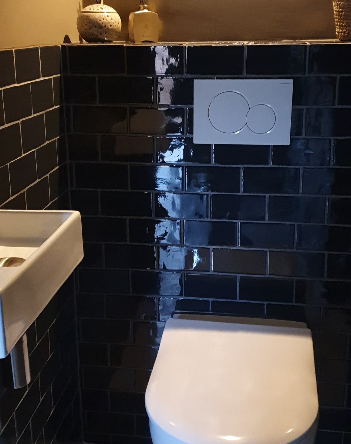 Toilet met glanzend zwarte metrotegels, wit bedieningspaneel en hangend closet